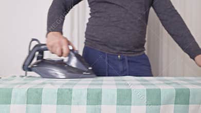 Close-up of a person ironing a green checkered tablecloth on an ironing board