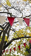 Red and white triangular bunting hanging against a background of bright yellow autumn foliage and sky