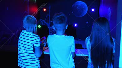 Teenage children shoot laser weapons at colored targets in the dark playroom.