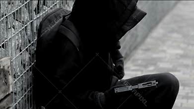 unrecognizable killer, bandit, or man in a hood and mask leaning against a wall, in ambush, reloading a pistol magazine