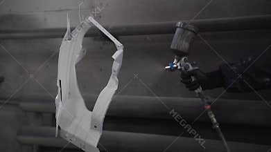 A car painter paints a part in a paint booth using a spray gun.