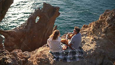 Adventurous Couple Enjoying Romantic Cliffside Picnic Overlooking Sparkling Ocean