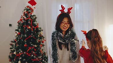 A daughter joyfully wraps her mother in sparkling garlands beside a festive Christmas tree, creating playful holiday memories in