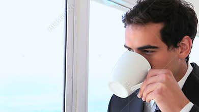 Man in a suit looks out the window then drinks