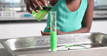Child is tilting beaker and pouring green liquid into cylinder to show foam reaction and overflow