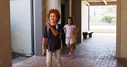 Diverse children stepping from doorway walking toward lens on tiled path and adjusting backpacks