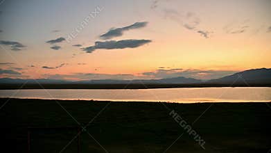 A ground-based panorama of a lake at sunset amidst the steppe with mountains in the background. Smooth panning.