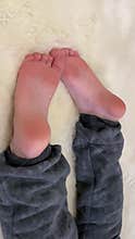 Close-up of barefoot child feet while boy lying on white fur and watching cartoons