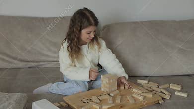 Young girl builds tower of wooden blocks on couch