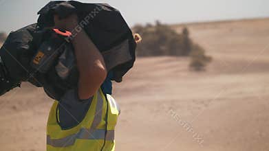A man carries a movie camera. filming in the desert. sandstorm