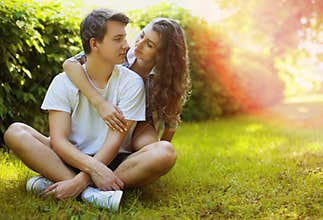 Lovely young teen couple in love having fun on lawn in park
