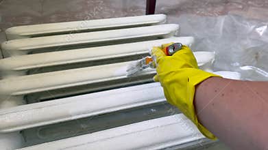 Hand in yellow glove painting old cast iron radiator