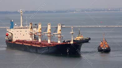 Cargo ship leaves port with tugs assistance
