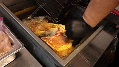 Chef wearing black gloves holding a seasoned pork chop on a metal tray, ready for the deep fryer