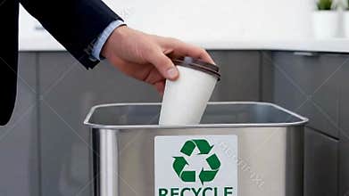 Close up of a person in a suit discarding a disposable coffee cup into a recycling bin emphasizing responsible waste disposal and