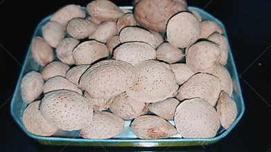 Extreme close up of almonds in a metallic tin with a single walnut centerpiece