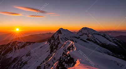 Snowy mountain peaks at sunrise with orange sky and sun rays mountains