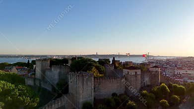 Drone view captures Sao Jorge Castle&#x27;s fortifications silhouetted against a vibrant sunset in Lisbon