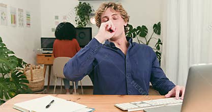 Tired Young Man Yawns While Working on Tech Startup Project in Diverse Office