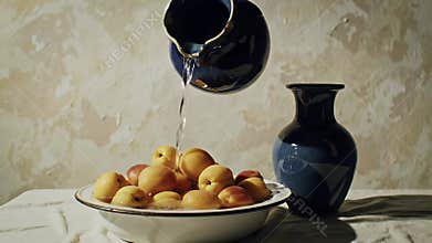 Bowl of Yellow Peaches Poured by Hand from Blue Jug on White Tablecloth Still Life