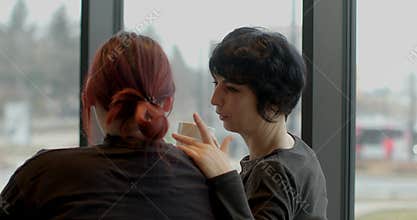 caucasian friend and stylist chatting by window during city break