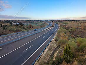 Road stretches through open land in a rural area during late afternoon with clear sky and few clouds