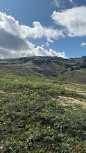 Expansive Green Meadow with Dramatic Clouds and Mountain Backdrop in Iceland