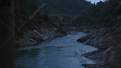River among rocks and an old arched bridge at dusk