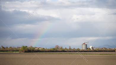 Faint rainbow appearing over a rural agricultural landscape with a silo