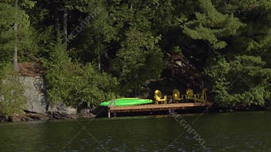 A wooden dock in a shaded forest with a green kayak and Adirondack chairs