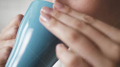 Girl is drinking hot coffee. Female hands bring mug of hot coffee to their mouths and drink. Close-up