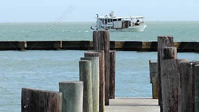 Wooden posts of a pier as an oyster boat sails on the water beyond the concrete breakwater
