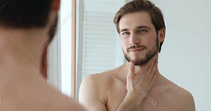 Confident bearded man applying aftershave lotion on face and neck