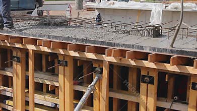Riggers, workers are holding pump hose to pouring fresh concrete and using electric vibratory to compact him in wooden mold