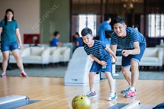 Father teaching son and family play bowling at bowling club on relax time, family activity on holiday concept