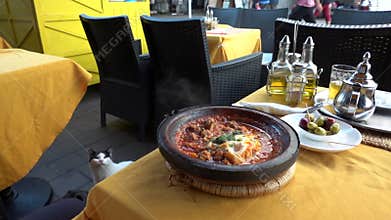 Traditional moroccan Tajine food cooking in pots on table in cafe and cat enjoying the view. Hand of local Cook is