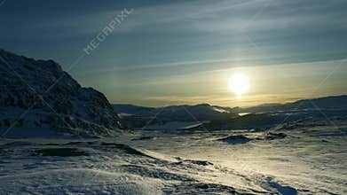 Time lapse of sunset in Scandinavian mountains, huge Sun with round winter halo goes down in Norway, clear blue sky with some