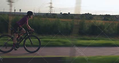Woman cyclist is riding fast from saddle, pushing pedals on bike up and hard training. Professional triathlete is speeding on bicy