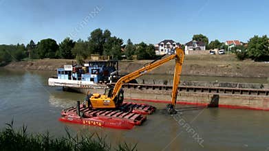 An excavator on the pontoon for cleaning the river bottom is waiting for the river barge for loading sludge and mud