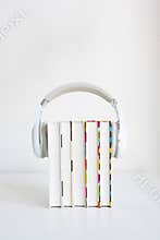 white headphones on a stack of 5 books on a table against a white wall background. audiobook concept.