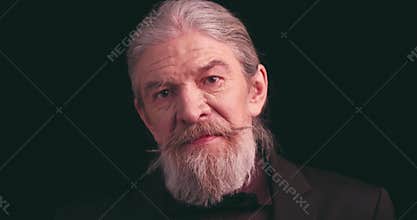 Old bearded male in classic clothes looking in camera on black background. Elderly stylish man model portrait in suit