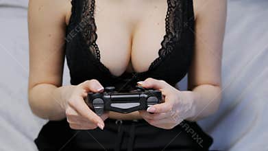 Close-up shot of sexy unrecognizable woman in a lace bra with gorgeous breasts playing games on the console on gamepad