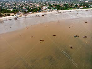 An aerial shot from Bagamoyo, Tanzania. Indian Ocean Coast with Vessels and Crowd of people Carrying Catch from