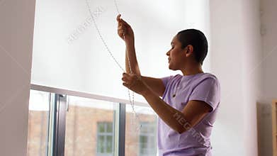 African woman closes window blinds at home