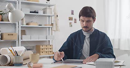 Handsome guy drawing on tablet and creating picture while sitting at his cosy workplace.Young man graphic illustrator