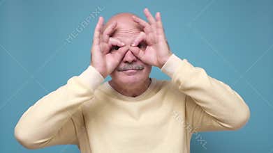 Senior man holding fingers near eyes like glasses or mask like super hero.