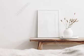 Portrait white frame mockup on vintage wooden bench, table. Modern white ceramic vase with dry Lagurus ovatus grass and