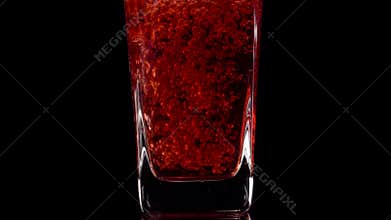 Premium Drink. Super slow motion shot of pouring pomegranate juice into a transparent glass against black background