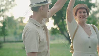 Happy mid-adult couple dancing at sunset in summer park. Portrait of positive smiling husband and wife dating outdoors