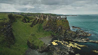 Irish castle cliff shore aerial view: Dunluce on green grass valleys and meadows at ocean bay